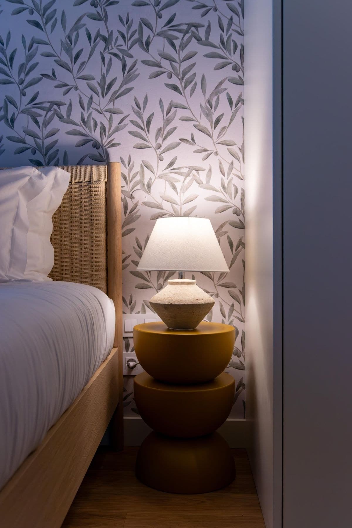 Cane Table Lamp, lit, on a bedside table